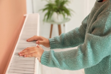 Photo of Child warming hands on heating radiator indoors, closeup