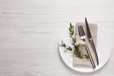 Stylish setting with cutlery and eucalyptus leaves on white wooden table, flat lay. Space for text