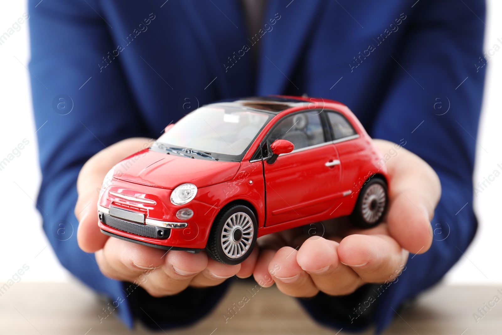 Photo of Insurance agent holding toy car over table, focus on hands