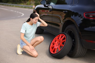 Tire puncture. Stressed woman with new wheel near car on roadside outdoors