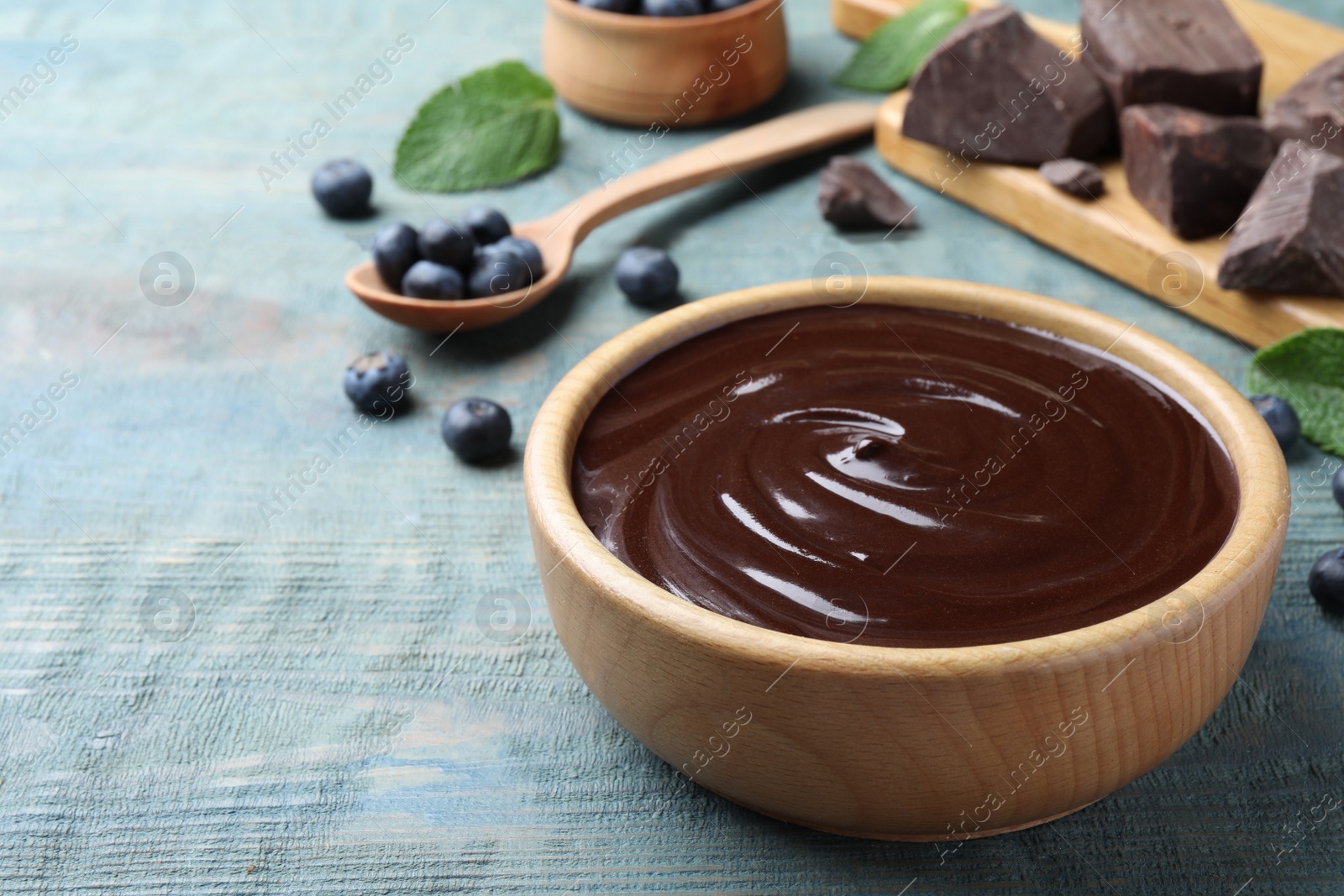 Photo of Delicious chocolate cream with blueberries on light blue wooden table, space for text