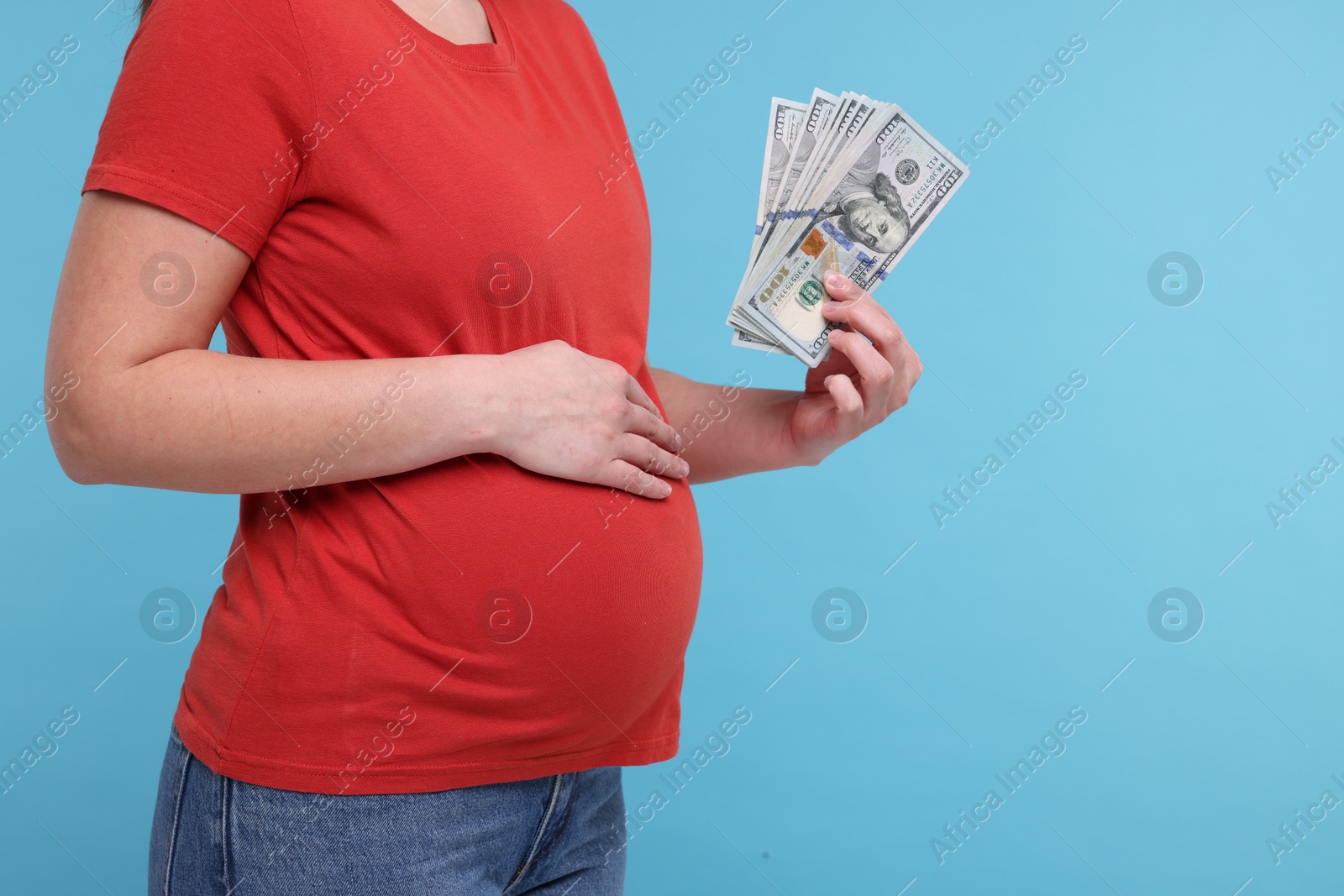 Photo of Surrogate mother. Pregnant woman with dollar banknotes on light blue background, closeup. Space for text