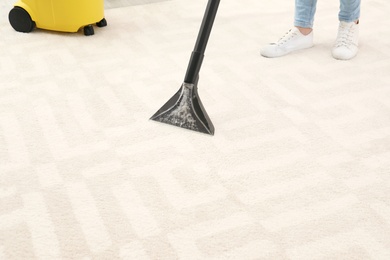 Photo of Woman removing dirt from carpet with vacuum cleaner indoors, closeup
