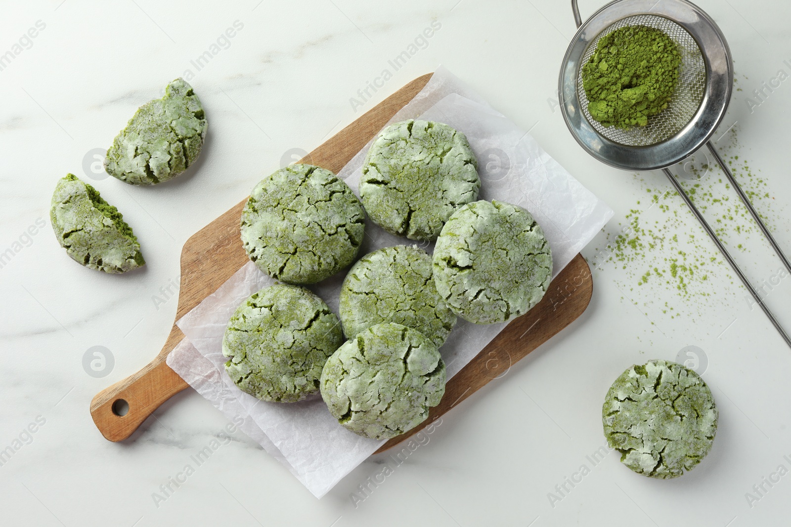 Photo of Board with tasty matcha cookies and powder on white marble table, flat lay