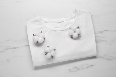 Photo of Fluffy cotton flowers and t-shirt on white marble background, top view