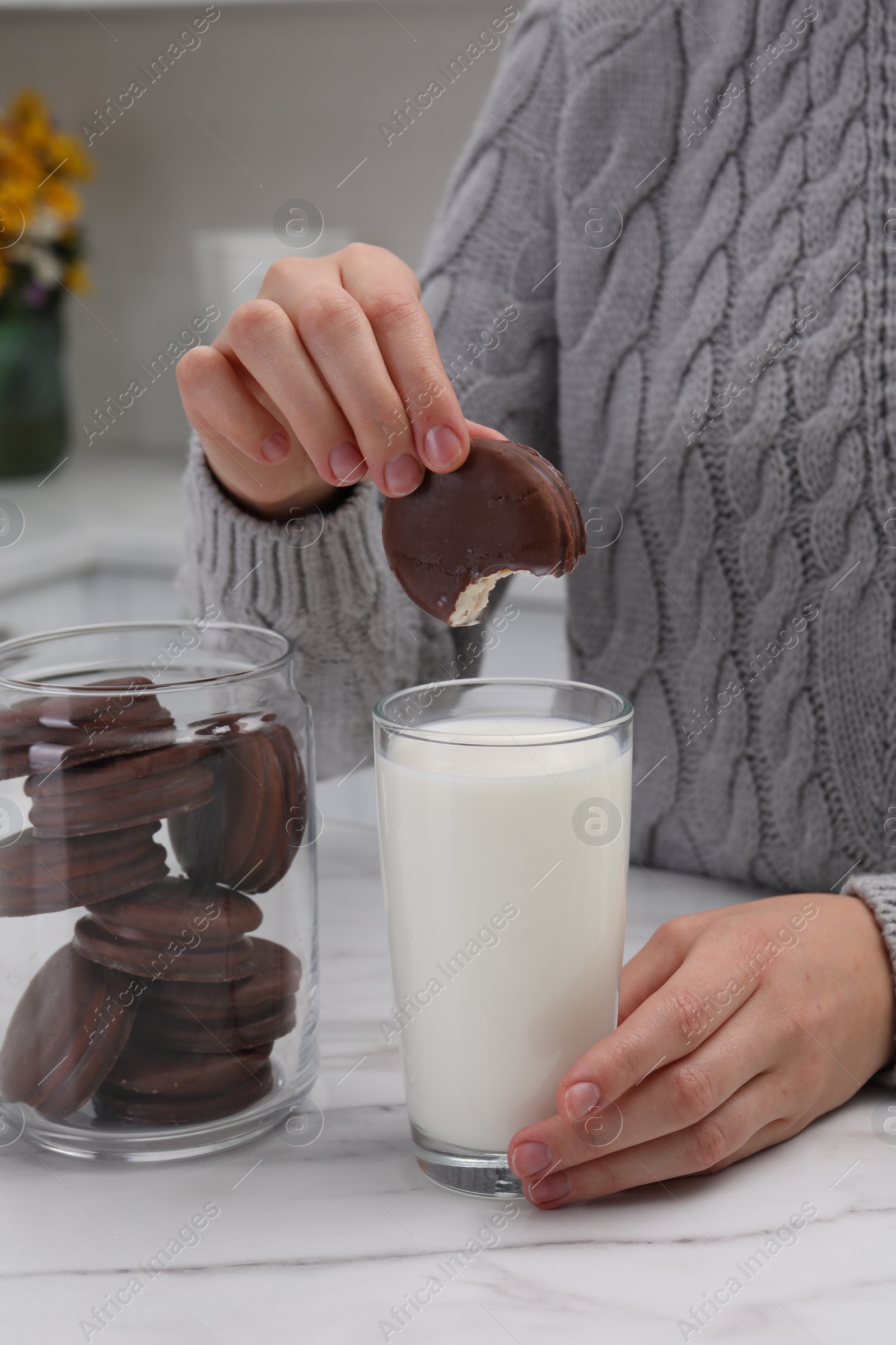 Photo of Woman dipping delicious choco pie into glass of milk at white marble table, closeup