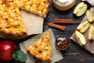 Photo of Traditional apple pie and ingredients on black wooden table, flat lay