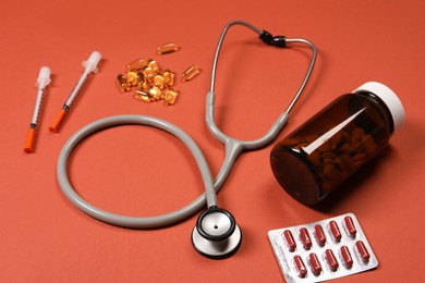 Photo of Stethoscope, syringes and pills on crimson background. Medical tools