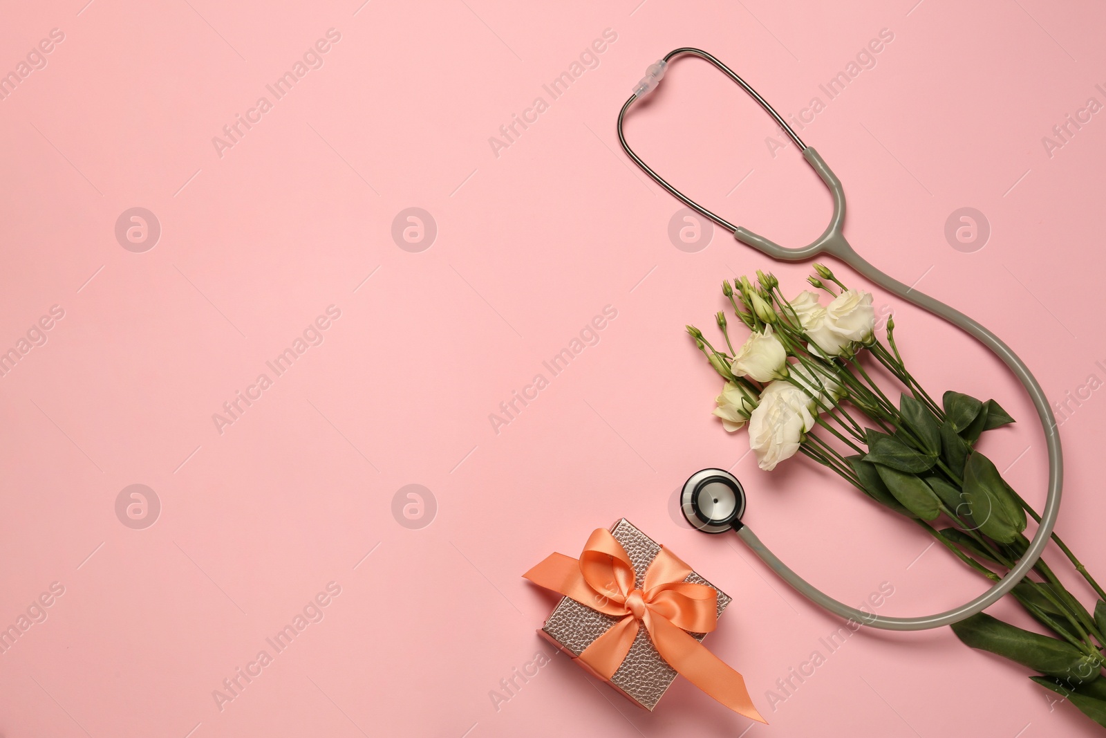 Photo of Stethoscope, gift box and eustoma flowers on pink background, flat lay with space for text. Happy Doctor's Day