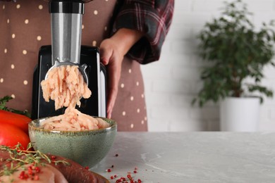 Photo of Woman making chicken mince with electric meat grinder at grey marble table indoors, closeup. Space for text