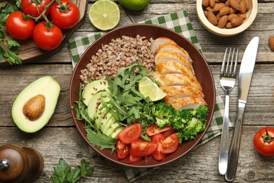 Photo of Healthy meal. Tasty products in bowl, ingredients and cutlery on wooden table, flat lay