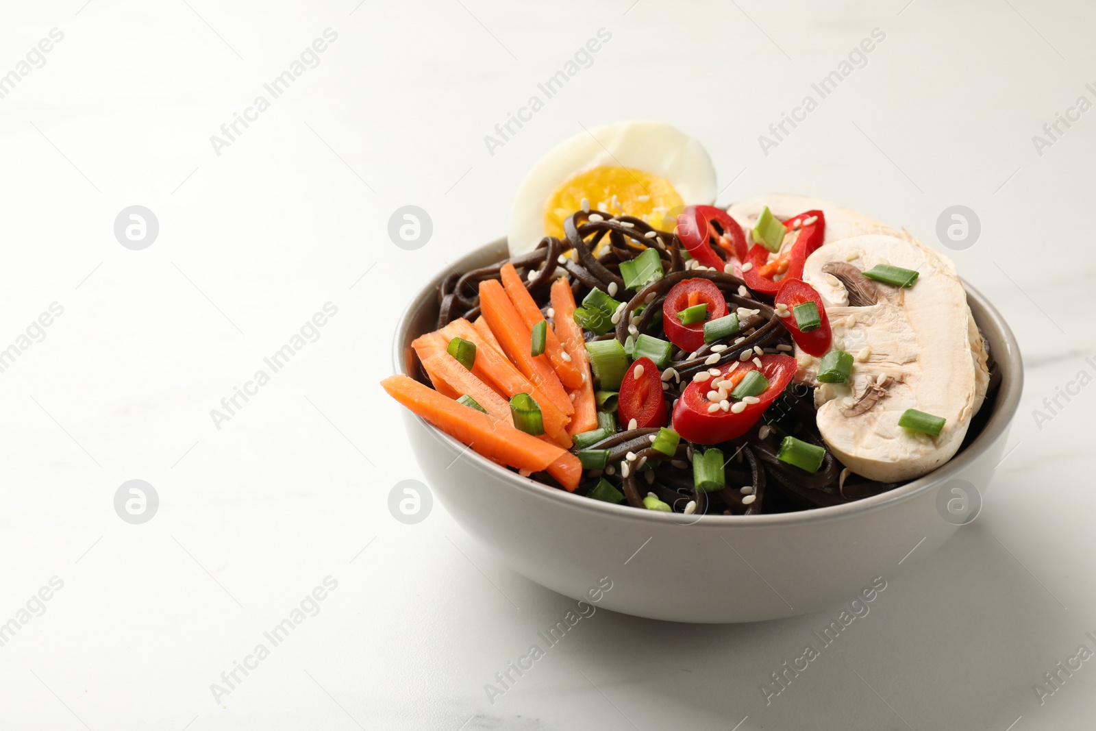 Photo of Tasty buckwheat noodles (soba) with chili pepper, egg, carrot and mushrooms on white marble table, space for text