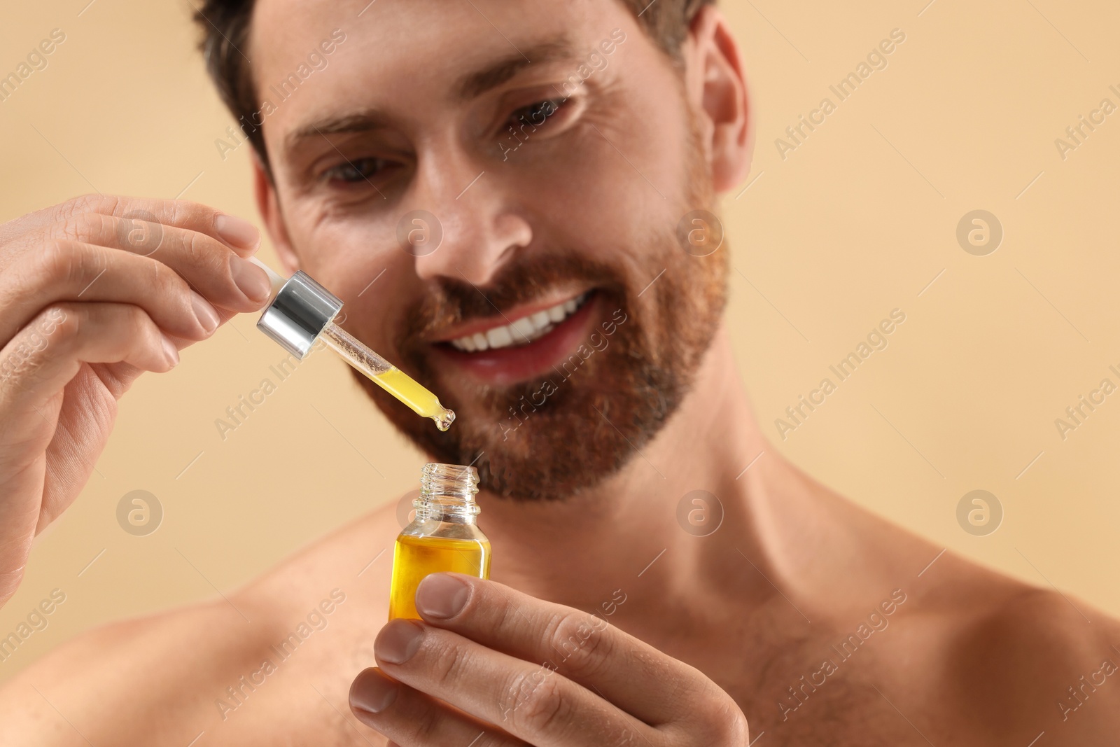 Photo of Smiling man with cosmetic serum on beige background, selective focus
