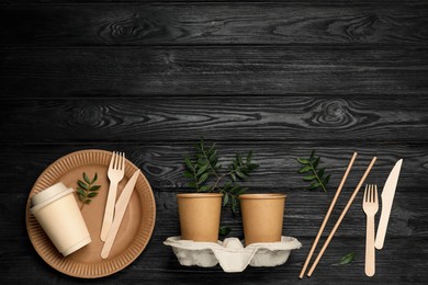 Photo of Flat lay composition with disposable tableware and green twigs on black wooden background. Space for text