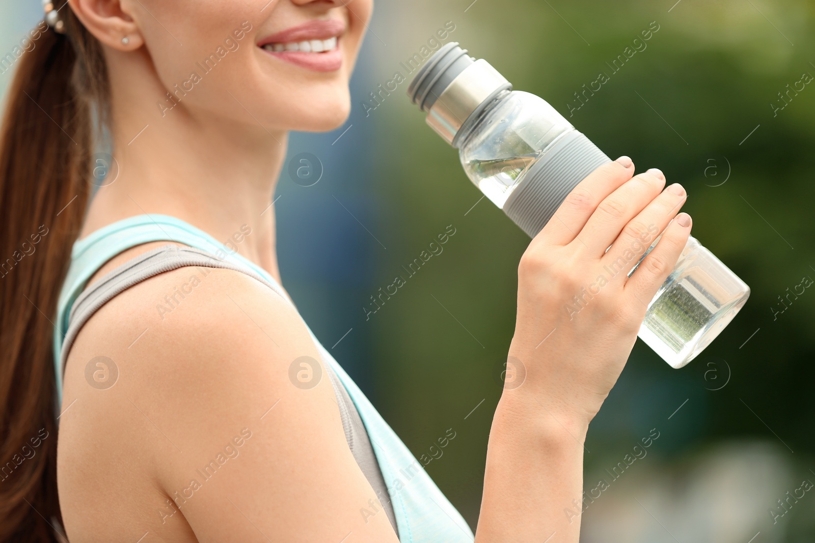 Photo of Young woman with bottle of water outdoors, closeup. Refreshing drink