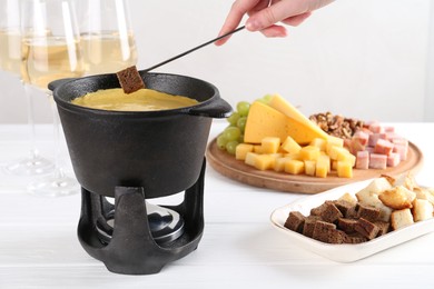 Photo of Woman dipping piece of bread into fondue pot with tasty melted cheese at white wooden table, closeup