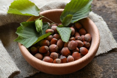 Tasty hazelnuts and green leaves on wooden table, closeup. Healthy snack