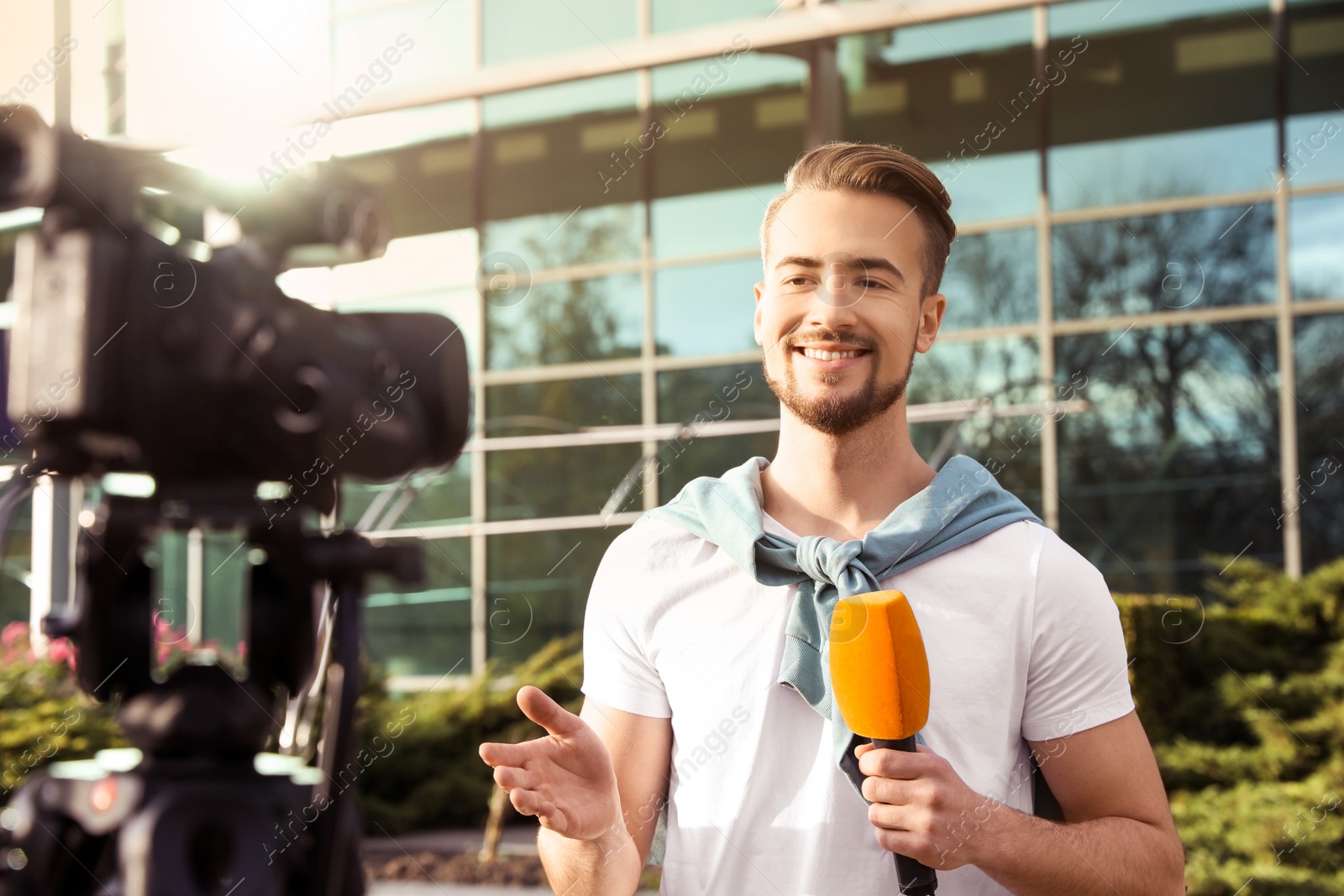 Image of Young male journalist with microphone working on city street