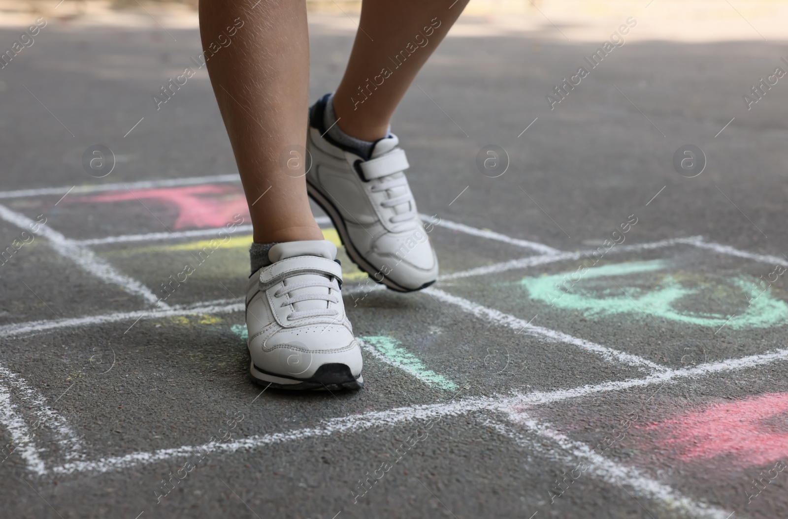 Photo of Little child playing hopscotch drawn with chalk on asphalt outdoors, closeup