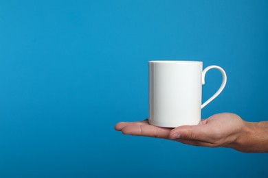 Photo of Man holding white mug on light blue background, closeup. Space for text