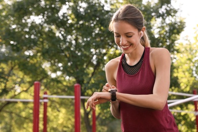 Photo of Young woman with wireless headphones and smart watch listening to music on sports ground