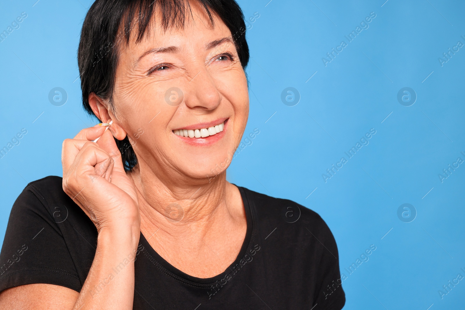 Photo of Senior woman cleaning ear with cotton swab on light blue background. Space for text