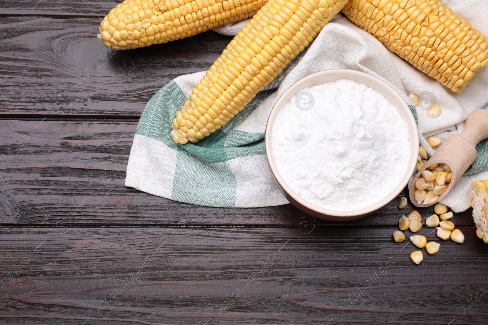 Photo of Bowl with corn starch, ripe cobs and kernels on dark wooden table, flat lay