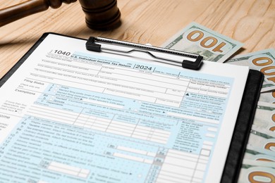 Photo of Clipboard with tax return form, dollar banknotes and gavel on wooden table, closeup