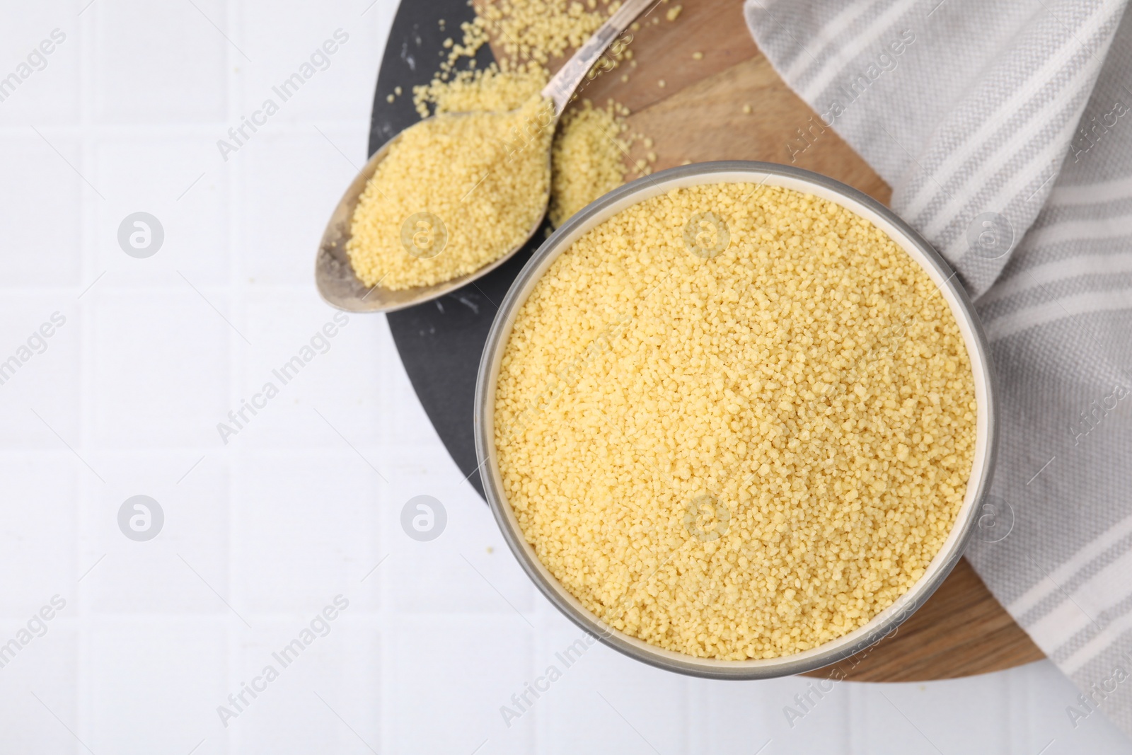 Photo of Bowl and spoon with raw couscous on white table, flat lay. Space for text