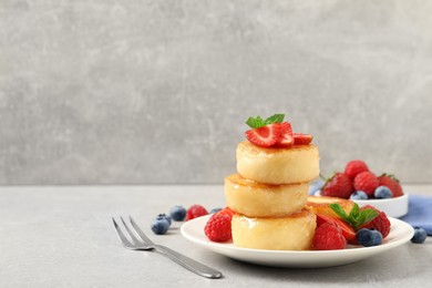 Delicious cottage cheese pancakes with fresh berries, mint and honey on light grey table, space for text