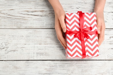 Photo of Young woman holding beautiful gift box on wooden background, top view