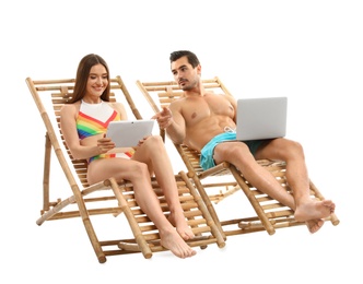 Young couple with computers on sun loungers against white background. Beach accessories