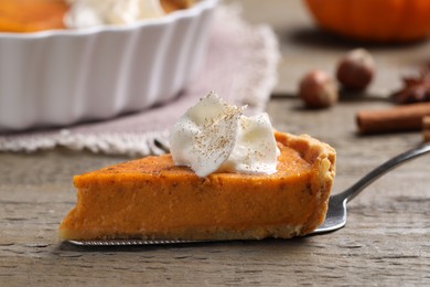 Piece of delicious pumpkin pie with whipped cream on wooden table, closeup
