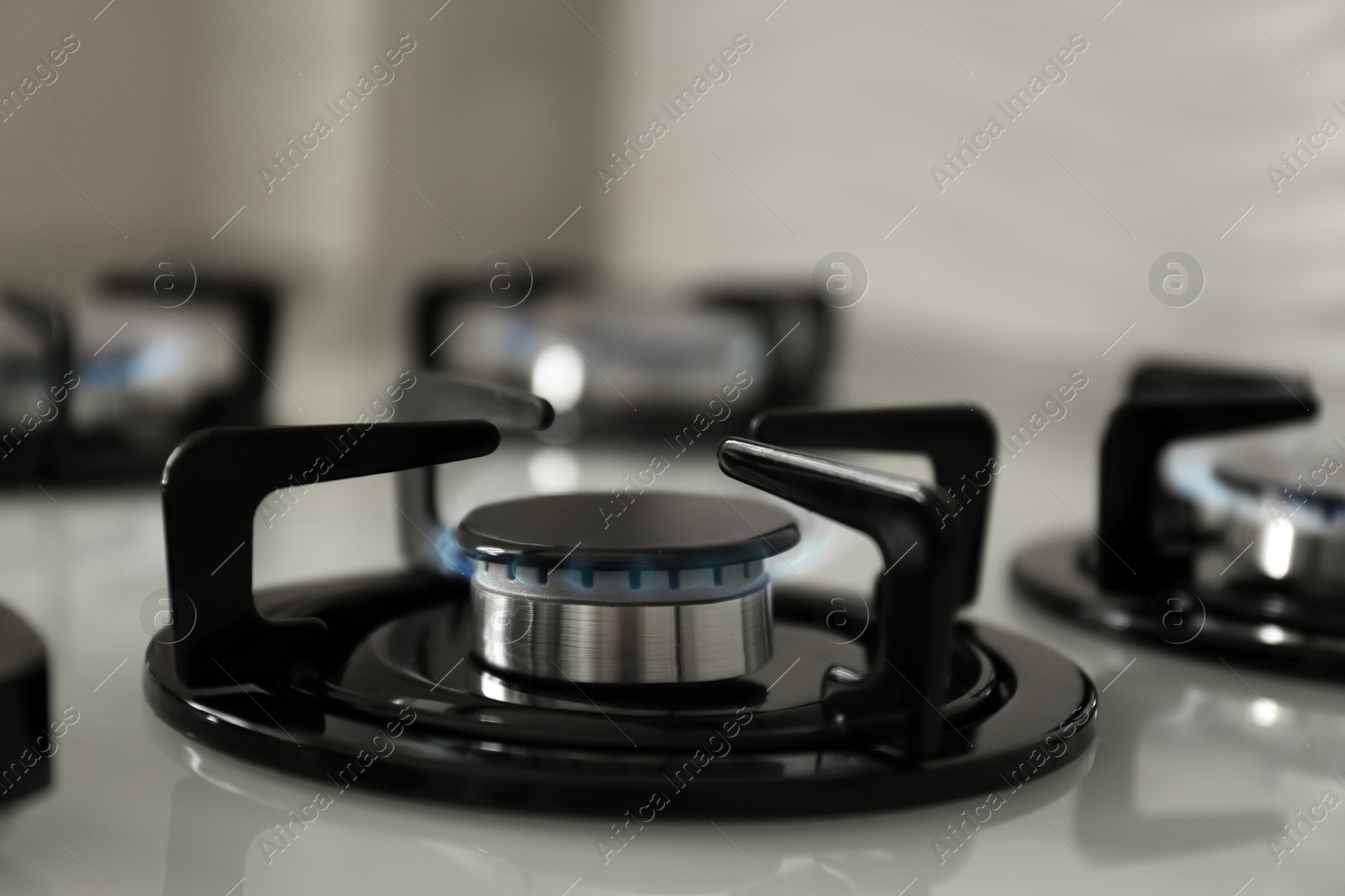 Photo of Gas burners with blue flame on modern stove, closeup