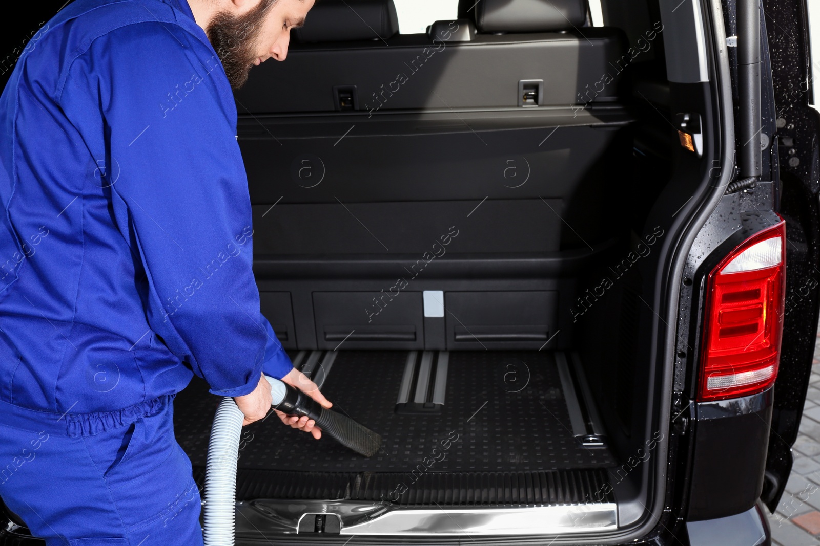 Photo of Worker using vacuum cleaner in automobile trunk at car wash