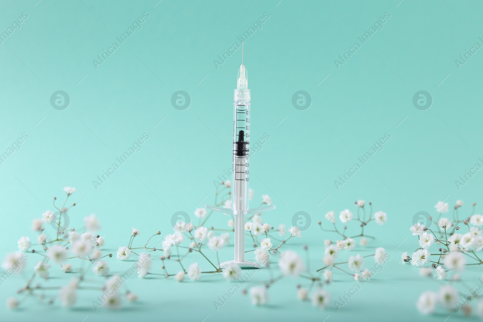 Photo of Cosmetology. Medical syringe and gypsophila flowers on turquoise background