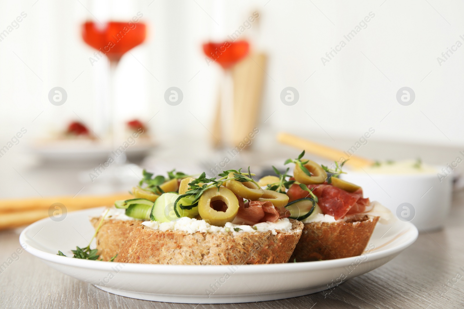 Photo of Plate of delicious bruschettas with prosciutto on grey wooden table