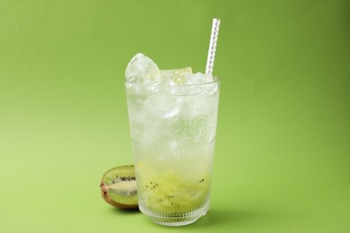 Glass of refreshing drink and cut kiwi on green background