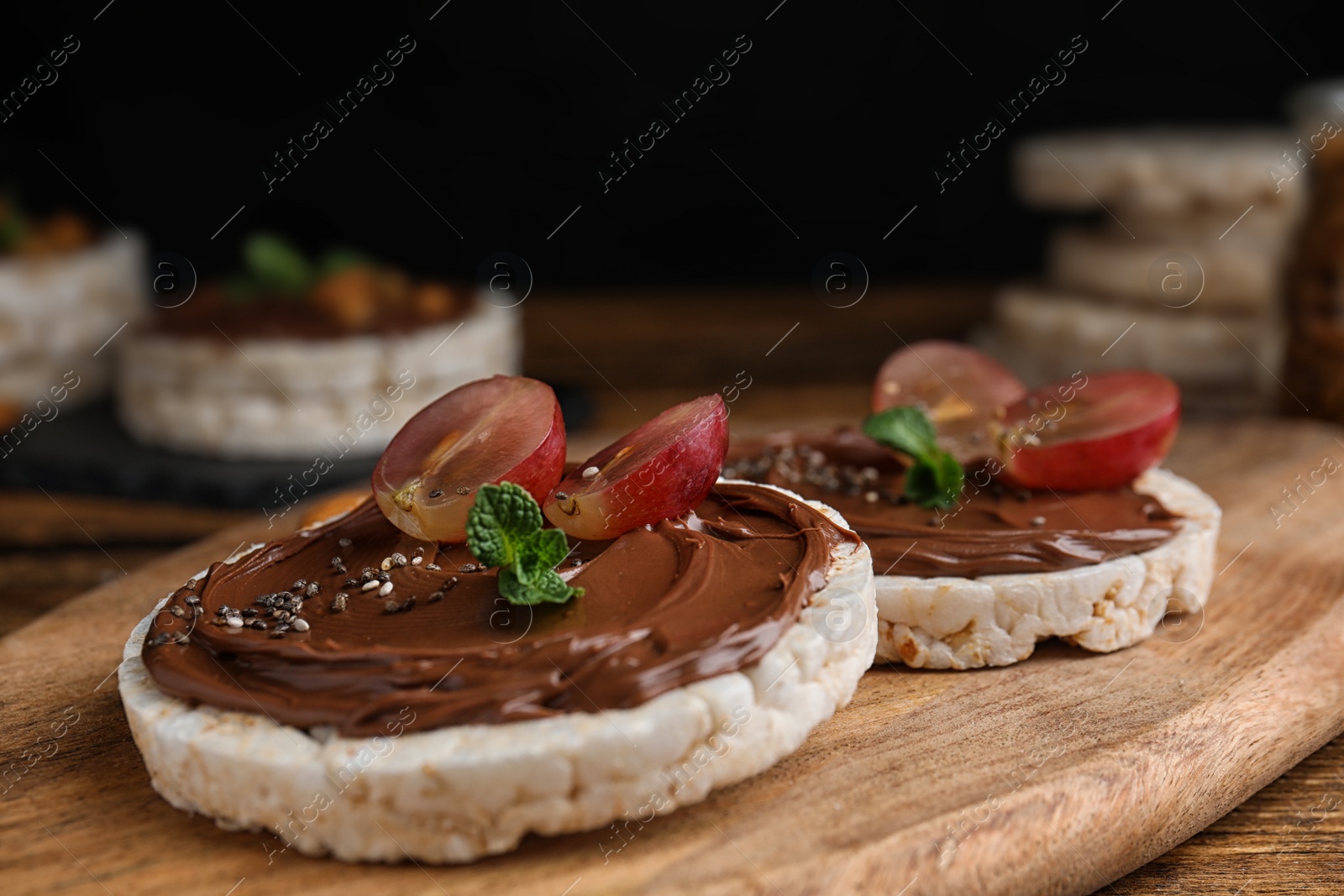 Photo of Puffed rice cakes with chocolate spread and grape on wooden board, closeup