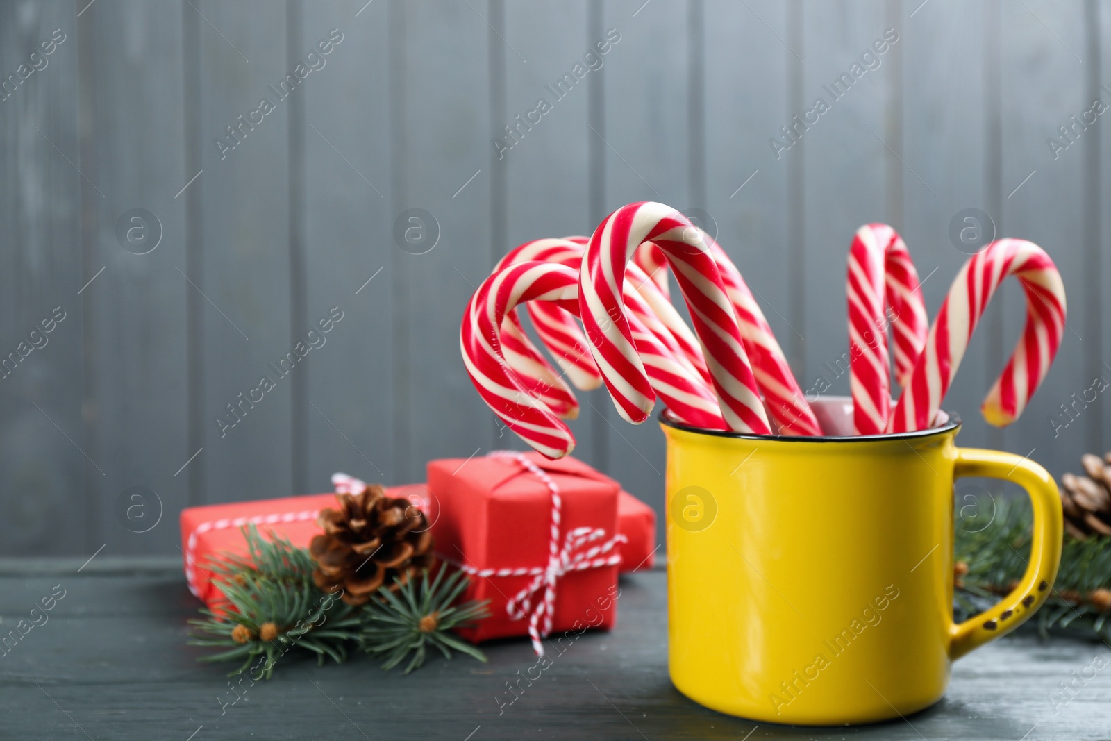 Photo of Many sweet candy canes in cup, gift boxes and Christmas decor on grey wooden table. Space for text