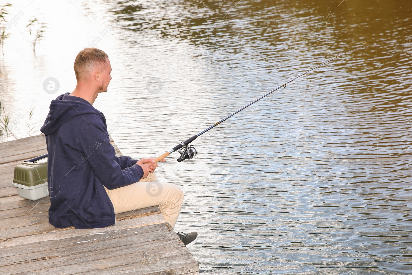 Photo of Man fishing on wooden pier at riverside. Recreational activity