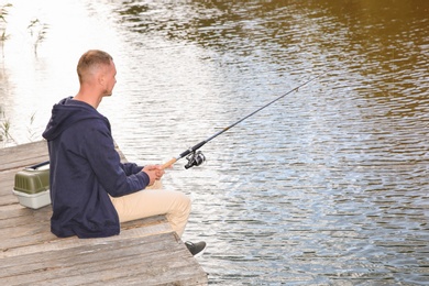 Man fishing on wooden pier at riverside. Recreational activity