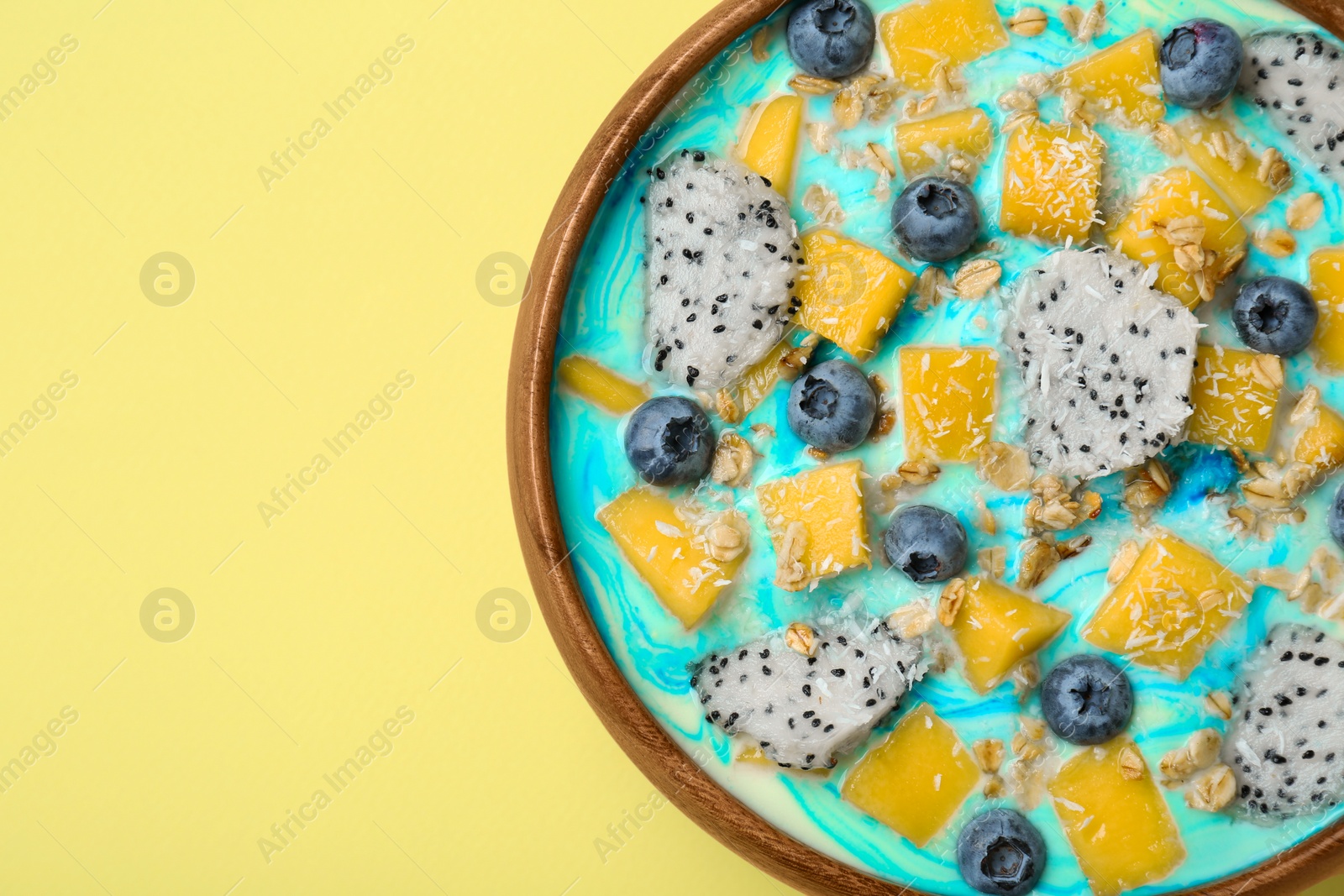 Photo of Delicious smoothie bowl with fresh fruits, blueberries and oatmeal on yellow background, top view. Space for text