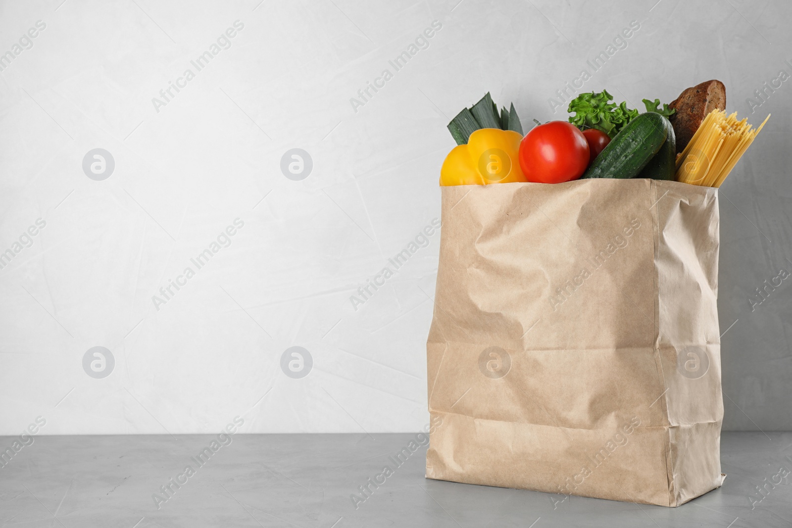 Photo of Paper bag with fresh vegetables on grey table against light background, space for text