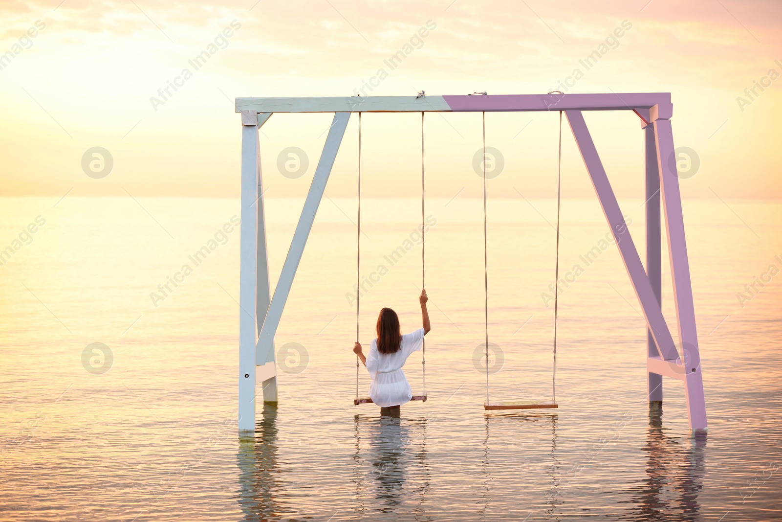 Photo of Young woman enjoying sunrise on swing over water