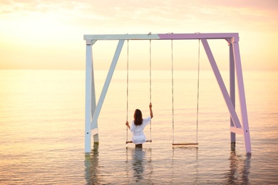 Young woman enjoying sunrise on swing over water