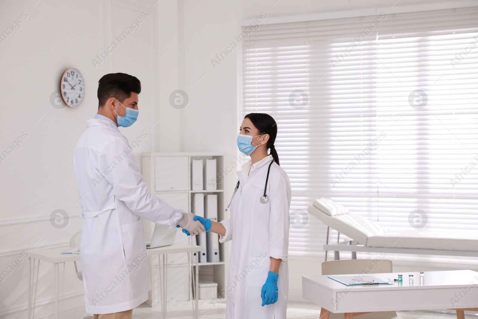 Photo of Doctors in medical gloves with protective masks giving handshake at hospital