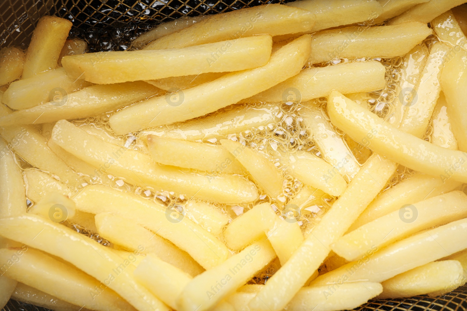 Photo of Cooking delicious french fries in hot oil, closeup