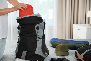 Photo of Woman packing different camping equipment into backpack at home, closeup