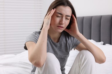 Sad woman suffering from headache on bed indoors